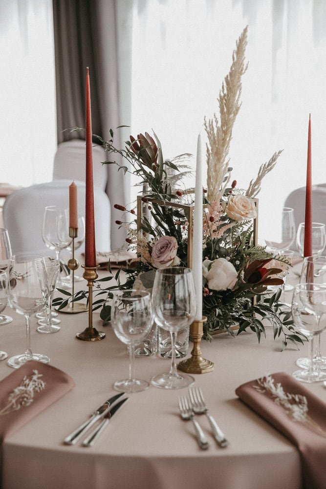 Įvairių gėlių puokštė vestuvių ar renginio dekoracijoms, sudaryta iš rožių, žolinių augalų ir elegantiškai papuošta žvakėmis.